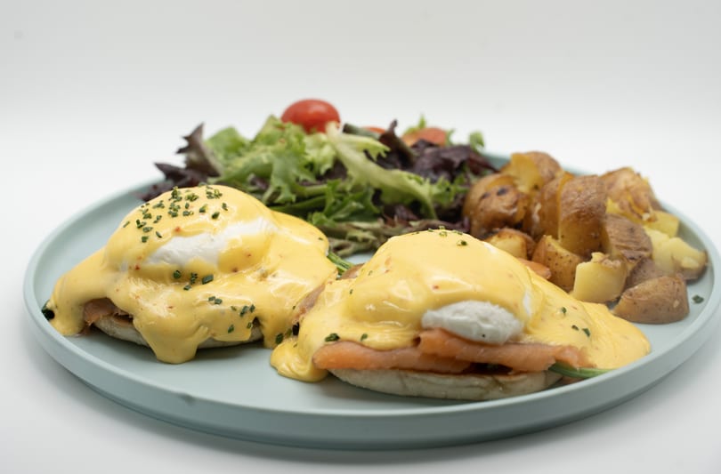 Eggs Benedict with smoked salmon, hollandaise sauce, chives, roasted potatoes, and a side salad.